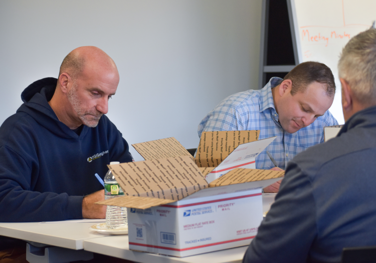 Three man sitting around a table with packaging boxes