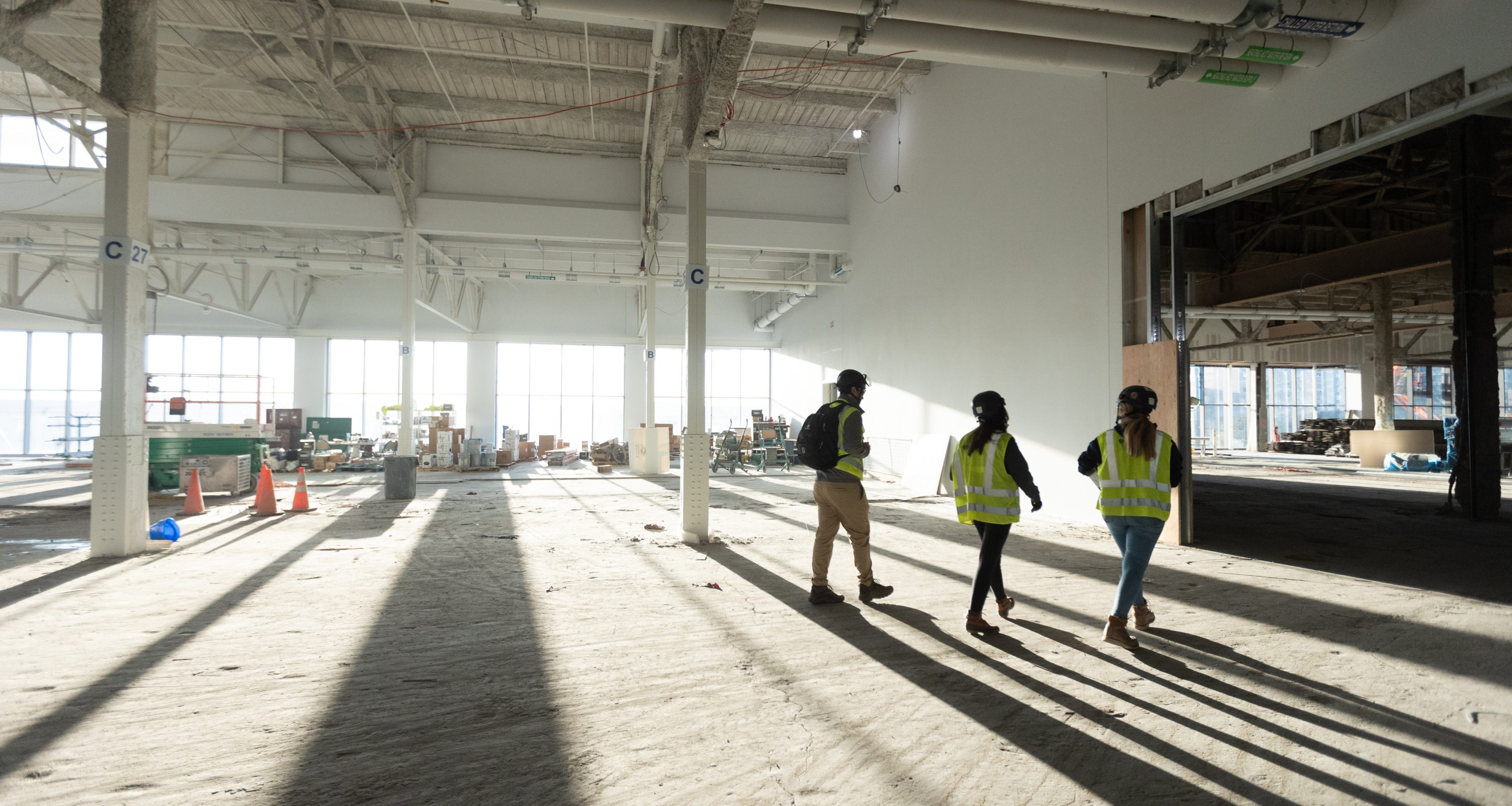 Three people in construction gear walking through a building under construction