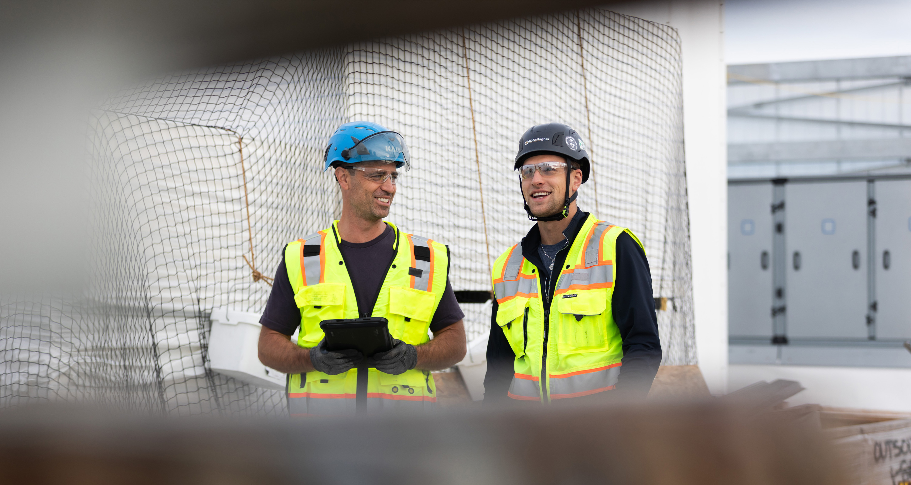 Two men in construction gear, standing, talking, and smiling