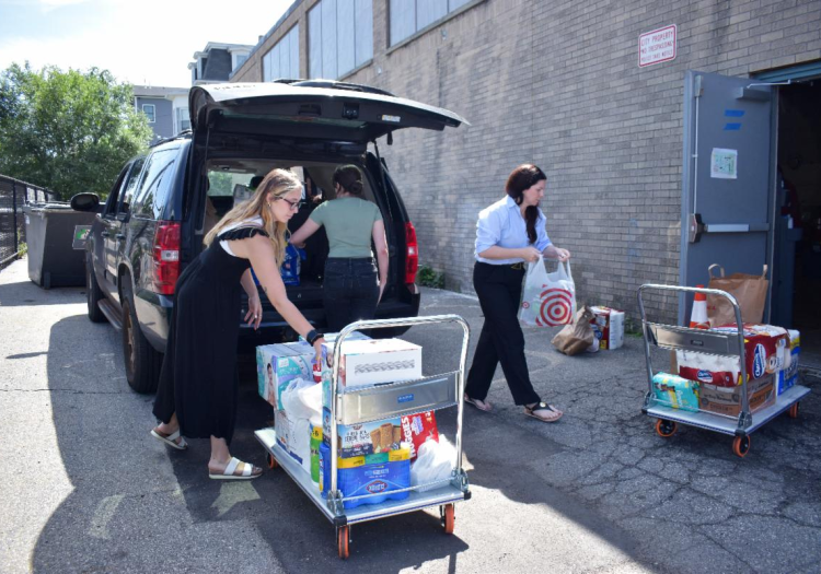 Three women carrying bags of groceries out of the trunk of a car